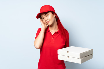 Pizza delivery girl holding a pizza over isolated background making sleep gesture in dorable expression