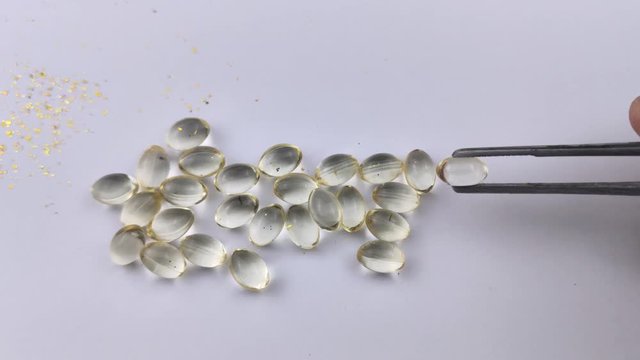 A man with tweezers takes one of Vitamin D3 capsules, brings it to the screen, and then takes it out of the frame. Capsules d3 isolated on a white background