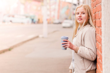 Portrait of young caucasian woman holding a cup of coffee against brick wall. Urban concept.
