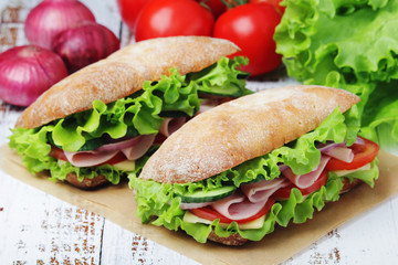 Two sandwiches with fresh vegetables, ham and cheese in ciabatta bread
