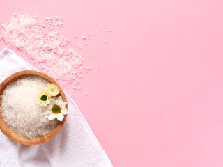 Spa flatlay composition. sprinkled and in jar sea salt, bath towel, flower on pink background. Copyspace, top view. Home body care concept