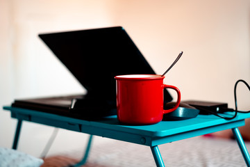 Work from home workspace set-up during Coronavirus pandemic. Red mug, laptop competer,portable hard disk and lap desk