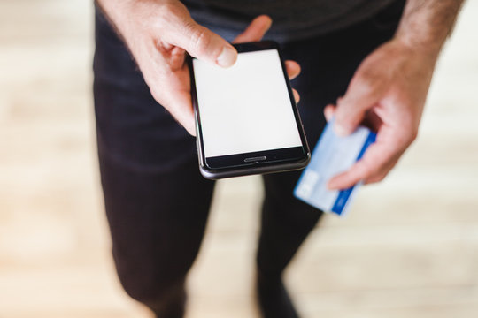 Man using smartphone with white screen for text and holding a credit card in hand. Online shopping concept during corona virus pandemic.