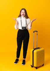 Full body of traveler teenager girl with suitcase over isolated yellow background unhappy and frustrated with something