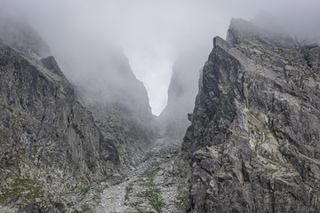 Mountain pass surrounded by fog, grey rocks in the mountains, passage between the peaks, invisible due to low clouds, in Tatra Mountains