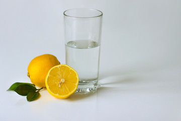 ripe yellow lemons and a refreshing glass of water on a white background
