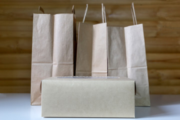 Three brown paper bags with handles and carton box on the wooden background
