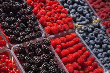 many plastic containers with berries: raspberries, blueberries, blackberries for sale.
