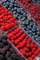 many plastic containers with berries: raspberries, blueberries, blackberries for sale.