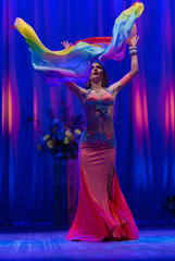 Dancer with long hair in orange neon  oriental costumes dance belly dance on the concert stage