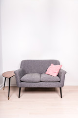 View from above of a cute gray settee with a pink pillow sitting on it, next to a small, contemporary occasional table. Portrait orientation with copy space on the wall.