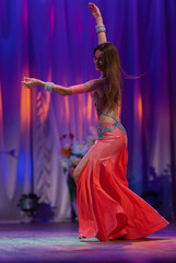 Dancer with long hair in orange neon  oriental costumes dance belly dance on the concert stage