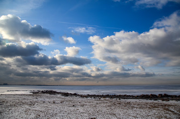 View of snow-covered sandy beach near the frozen Gulf of Finland.  Bright cloudy winter day on the outskirts of St. Petersburg