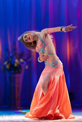 Dancer with long hair in orange neon  oriental costumes dance belly dance on the concert stage