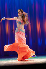 Dancer with long hair in orange neon  oriental costumes dance belly dance on the concert stage