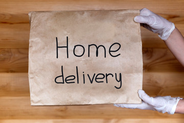 Hands in white medical gloves holding paper bag with "home delivery" written on it