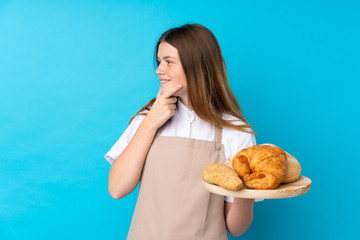 Ukrainian teenager chef uniform. Female baker holding a table with several breads thinking an idea and looking side