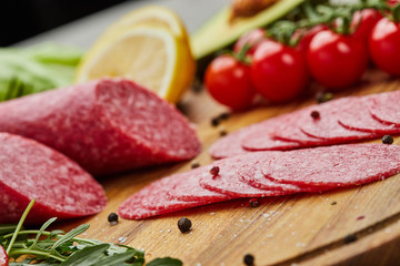 Traditional thinly sliced salami on a wooden cuttingboard  with spices, lettuce, avocado and tomatoes. Cold meat plate