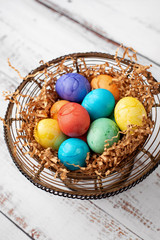 Brightly Colored Easter Eggs in a Wire Basket on a White Wood Table