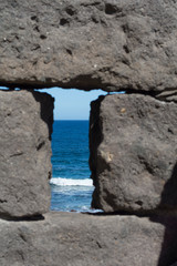 Between the gray stone blocks, you can see the blue sea in the background, illuminated by sunlight.