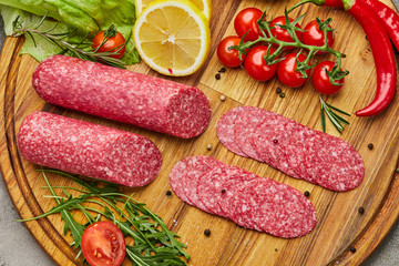 Traditional thinly sliced salami on a wooden cuttingboard  with spices, lettuce, avocado and tomatoes. Cold meat plate