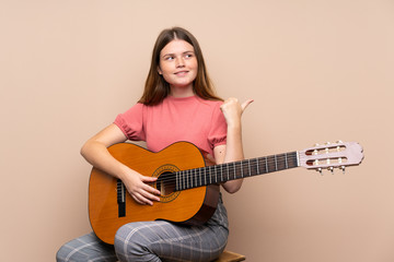 Ukrainian teenager girl with guitar over isolated background pointing to the side to present a product