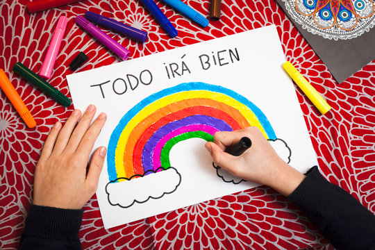 Girl's hands drawing rainbow picture in times of coronavirus with the phrase everything will be fine in Spanish