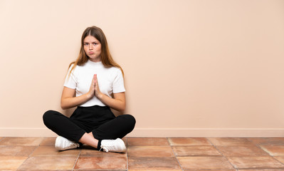 Ukrainian teenager girl sitting on the floor keeps palm together. Person asks for something