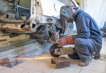 a car mechanic works angle grinder with a car body in a workshop. auto repair concept.
