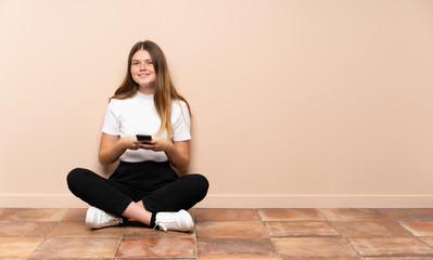 Ukrainian teenager girl sitting on the floor sending a message with the mobile