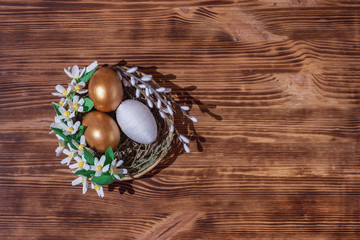 Fototapeta na wymiar Easter eggs in basket filled with straw and yellow flowers and willow on wooden rustic vintage background. Preparation for holiday. Easter decorations