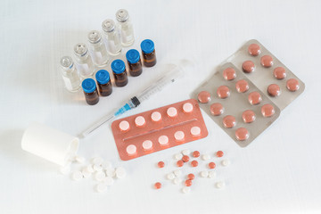 Scattered multicolored tablets, a syringe, and vials of medicine on a white table. Pharmaceuticals for the treatment