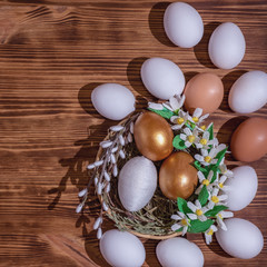 Easter eggs in basket filled with straw and yellow flowers and willow on wooden rustic vintage background. Preparation for holiday. Easter decorations