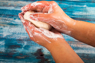 Fototapeta premium Someone is soaping their hands with a piece of toilet soap on a wooden background. Close up. Compliance with personal hygiene rules is the prevention of COVID-19 infection.