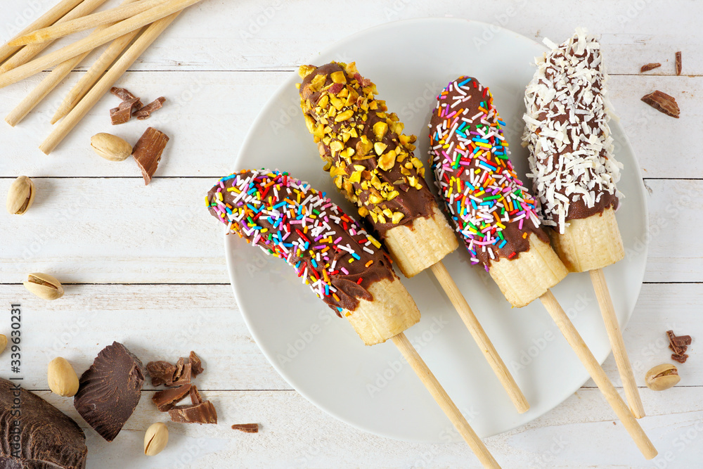 Aufkleber frozen chocolate dipped banana pops with sprinkles, nuts and coconut. overhead view table scene on a