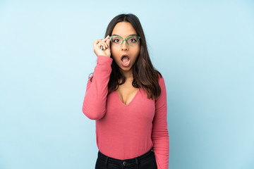 Obraz premium Young mixed race woman isolated on blue background with glasses and surprised
