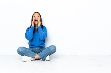 Young mixed race woman sitting on the floor isolated on white background shouting and announcing something