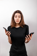 Fototapeta premium Portrait of a cute European brunette smiling woman in a black T-shirt, showing two cell phones for sales selection