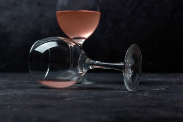 Two glasses with rose wine on a dark background. Half empty glass lies on its side. Wine tasting concept. Close up, copy space, law key