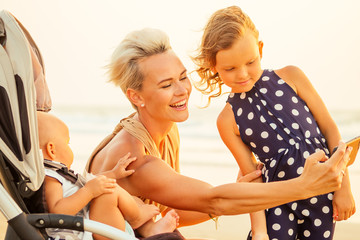 happy woman with two cute daughters outdoor making selfie portrait photo on smartpone camera frontal