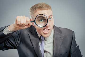 Fototapeta na wymiar Funny image of a adult man with a magnifying glass, one eye is enlarged.
