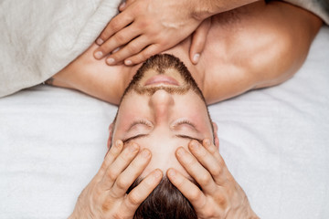 Fototapeta na wymiar Handsome young man receiving a relaxing head massage from a two masseurs in four hands in a health spa center.