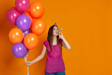 happy funny young woman in pink t-shirt and birthday hat with bright colorful air balloons blowing...