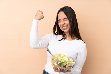 Young brunette girl holding a salad over isolated background celebrating a victory