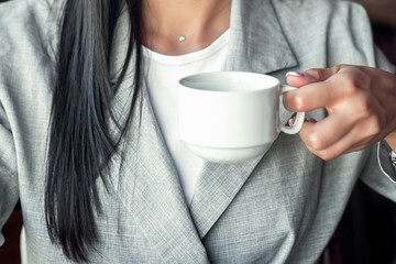 Young businesswoman is holding a white cup of hot drink wearing jacket, close up.
