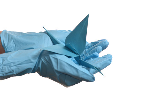 Origami paper crane in hand with rubber gloves over white