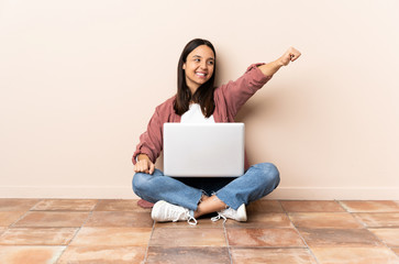 Young mixed race woman with a laptop sitting on the floor giving a thumbs up gesture