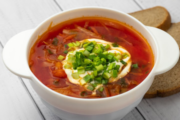 Beetroot soup in white bowl on light wooden table. Ukrainian, russian traditional cuisine concept. A national dish - borscht with sour cream and green onion.