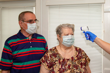 A doctor in blue latex gloves measures body temperature with an infrared emitter for a man and a...