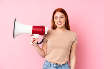 Young redhead woman over isolated pink background holding a megaphone